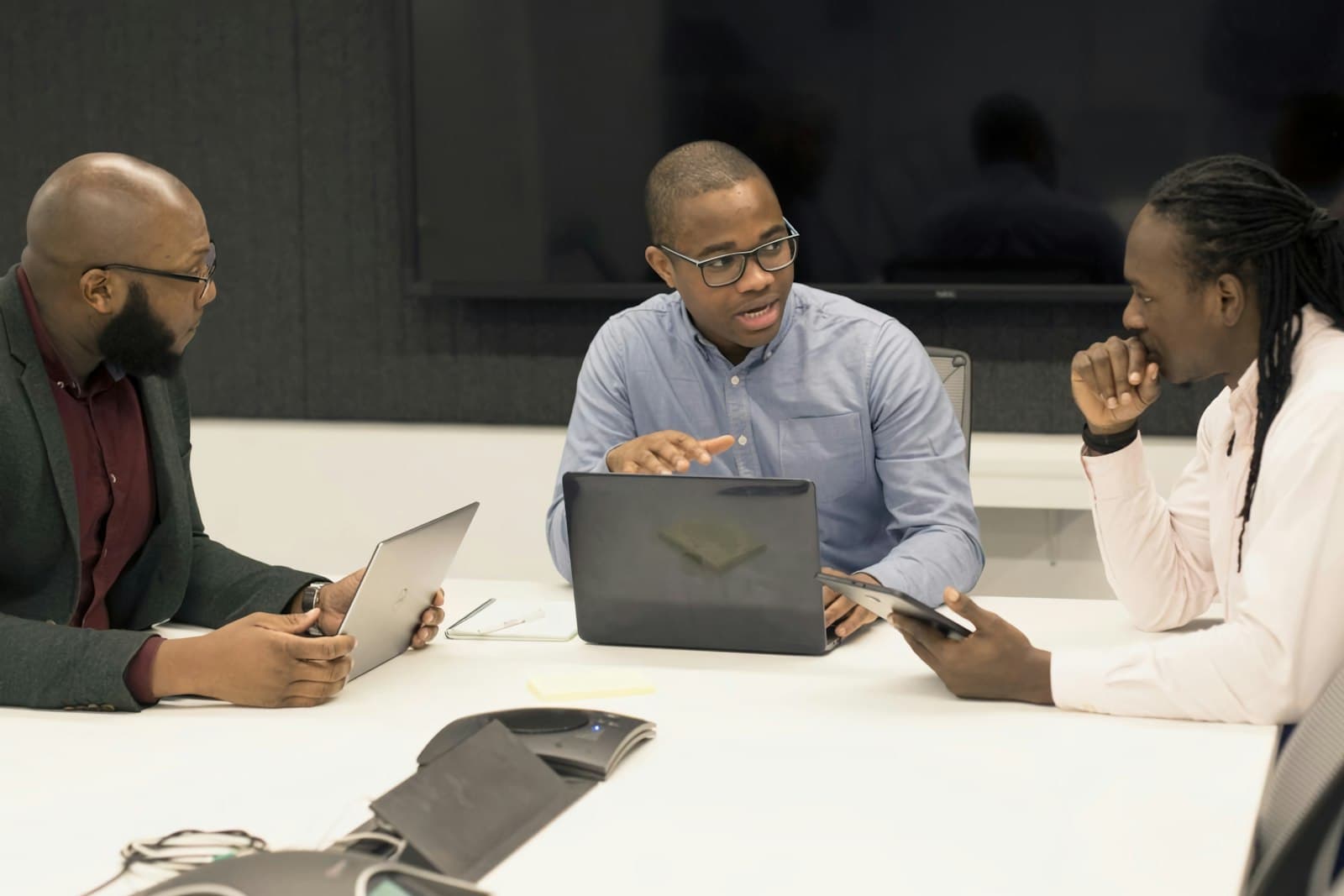 Three businessmen reviewing invoices on a laptop and tablet around a meeting table