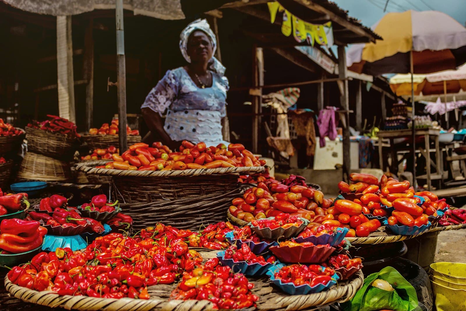 A trader standing behind baskets of peppers at a busy open market