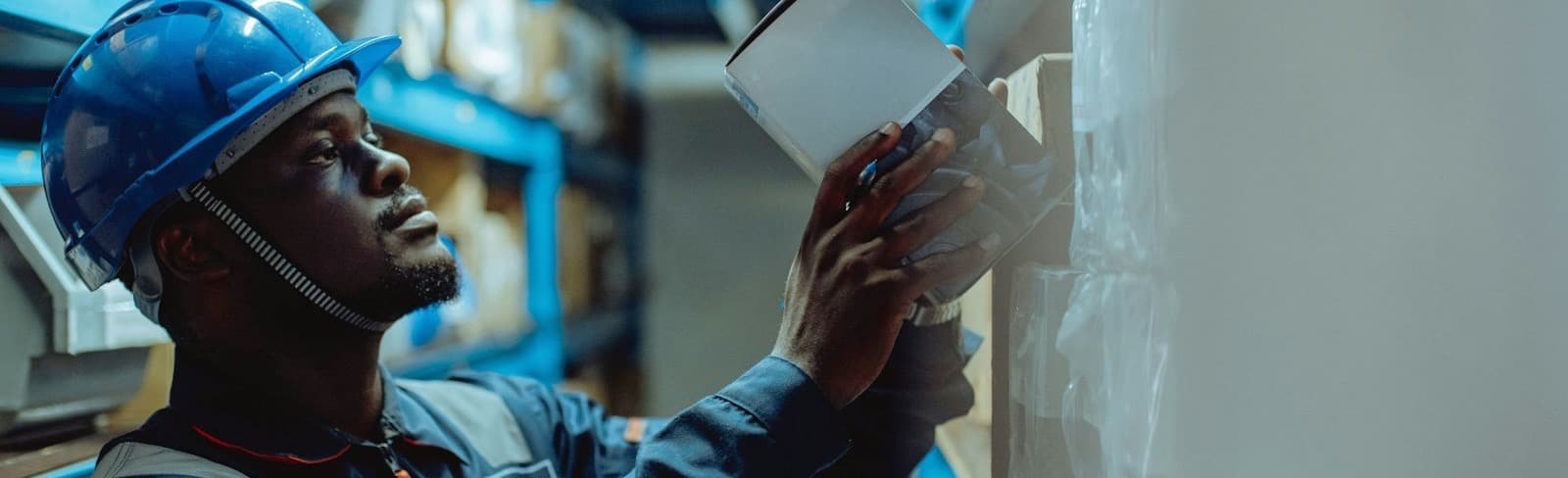 A warehouse worker in a hard hat checking stock on a shelf